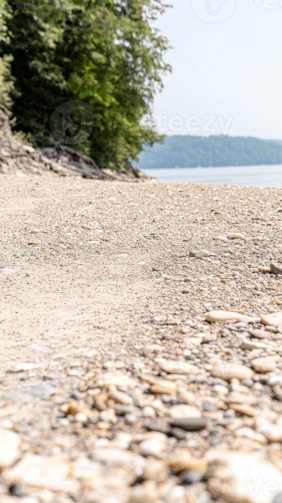 Tranquil Pebble Shoreline by Serene Lake with Lush Green Foliage and Distant Hills on a Bright Summer Day, Natural Outdoor Landscape Scene photo