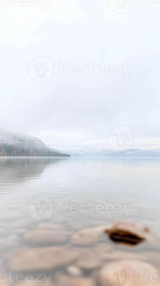 Misty Lake Serenity Tranquil Waters Reflecting Fog-Kissed Mountains and Clear Rocky Shoreline. A Peaceful Natural Landscape Vista. photo