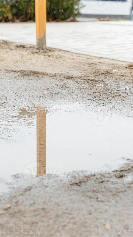 Serene Puddle Reflection on Wet Ground with Wooden Post in Urban Landscape. Tranquil Outdoor Scene Capturing Natural Elements and Still Water. photo