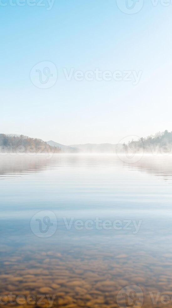 Tranquil Misty Lake at Dawn Serene Waters Reflecting a Clear Sky and Distant Autumn Hills photo