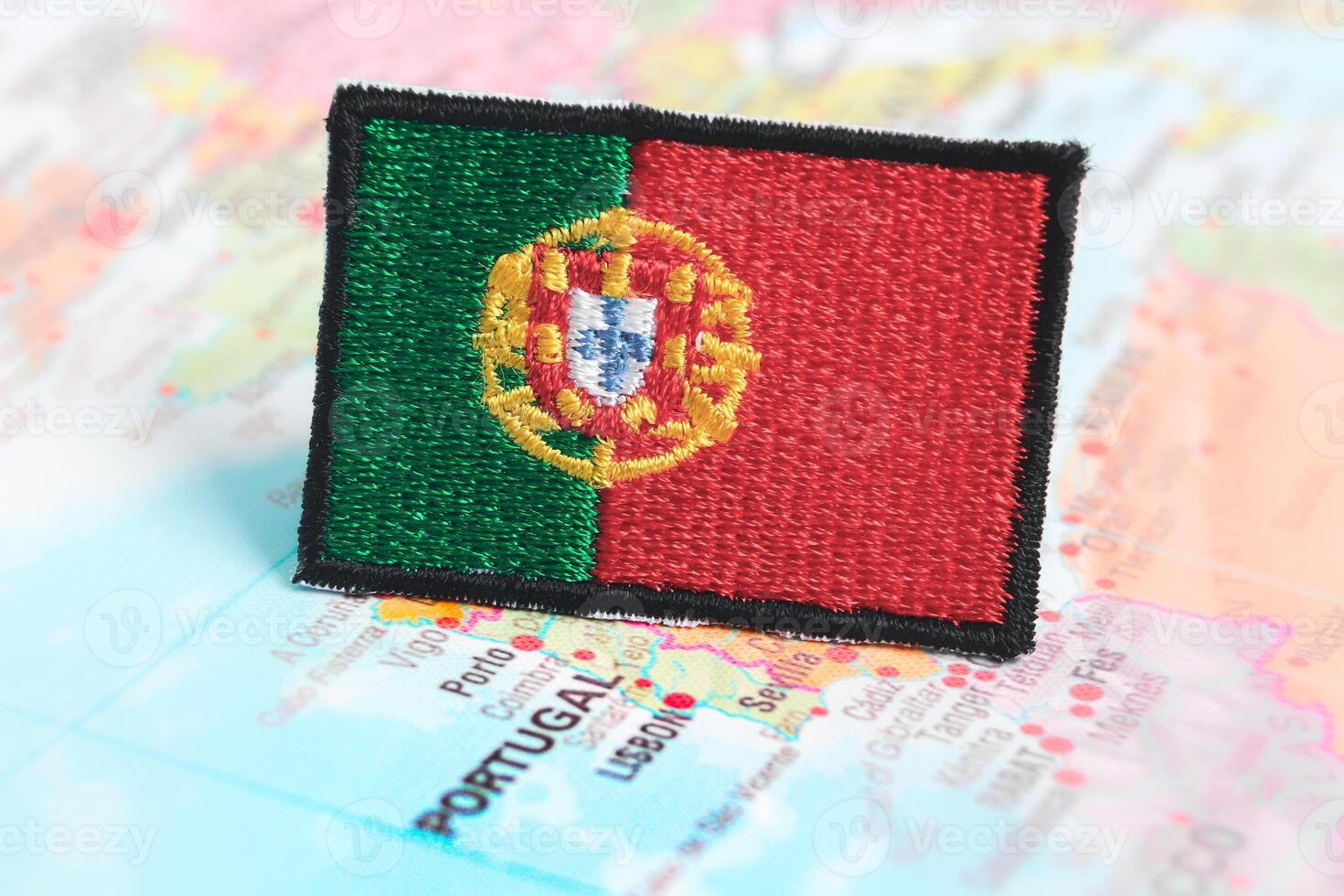 Close-up of hand-embroidered Portugal flag PT flag made from cloth and threads, positioned on a world map highlighting Europe and Portugal geographic spot. photo