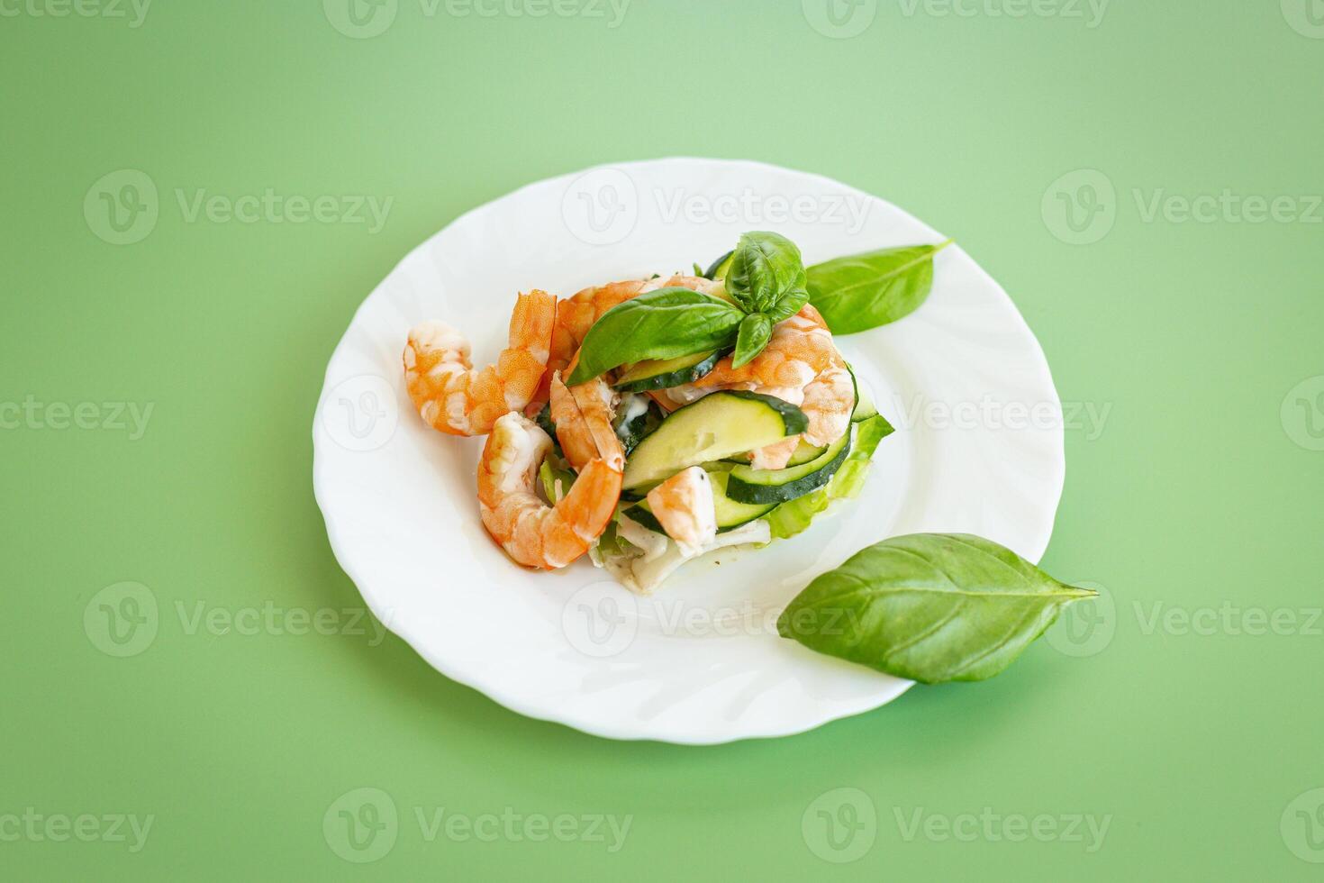 Fresh vegetable salad with shrimps and cucumbers on a green background . photo