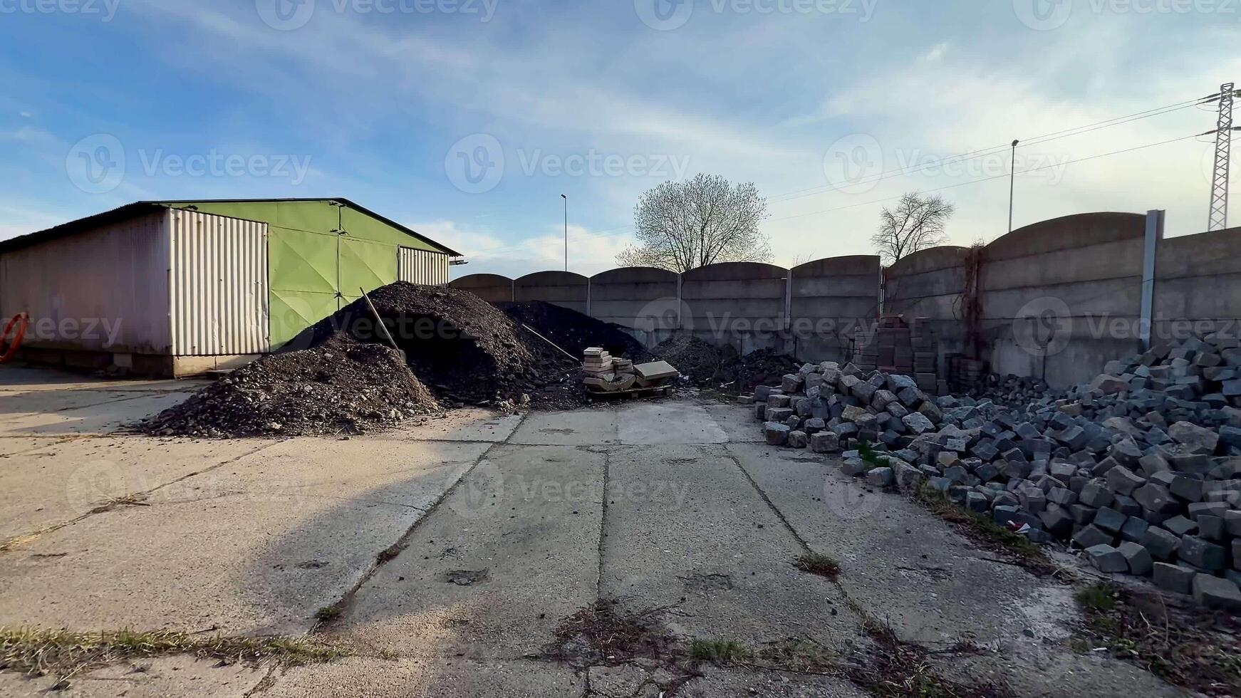 This storage site features large impressive piles of gravel and coal, enclosed by a sturdy fence under a clear blue sky photo