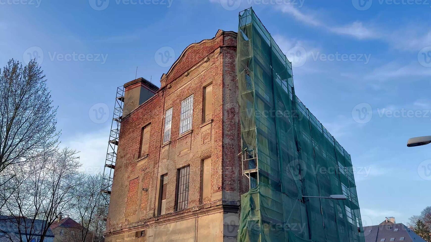 A historic brick building undergoing renovation, covered with green scaffolding, showcasing construction work. photo