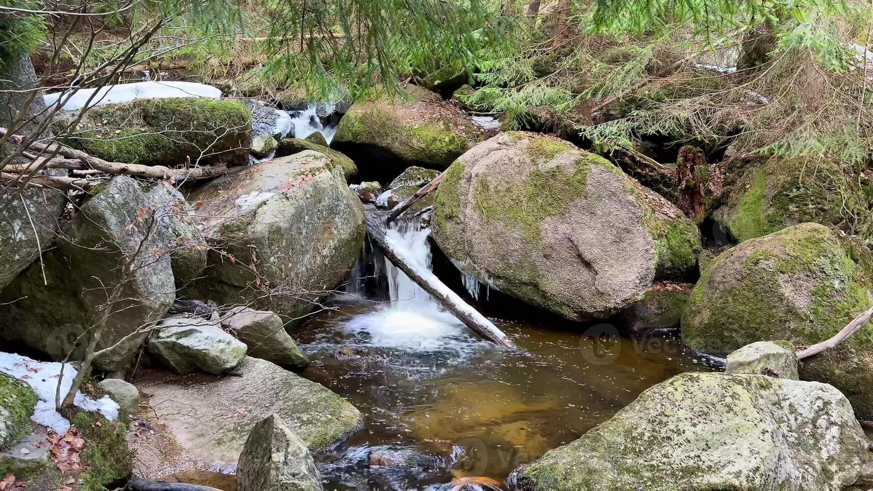 A gently soothing stream cascades gracefully over mosscovered rocks in a peaceful and serene forest setting photo