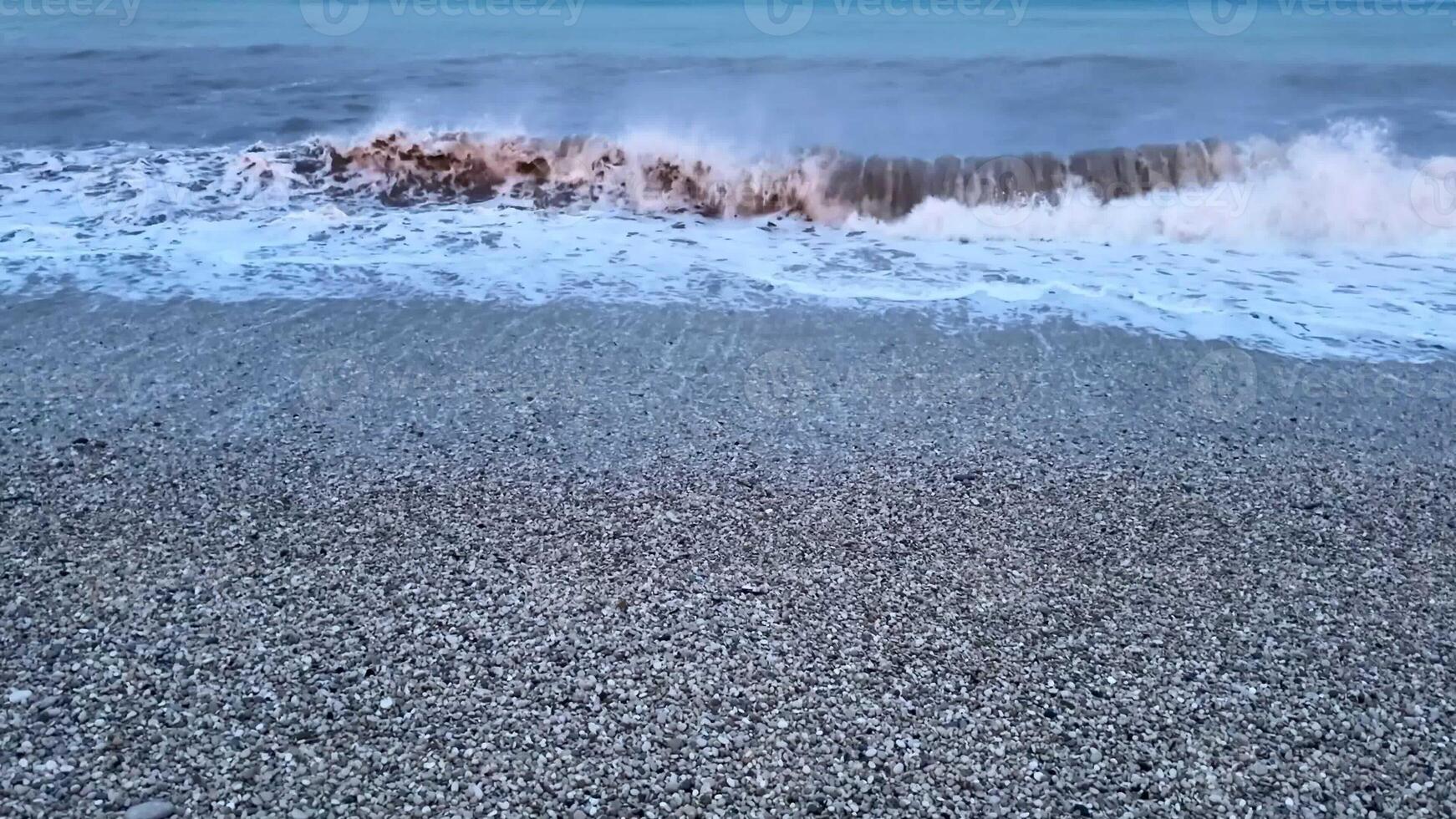 Immerse yourself in the serene and captivating beauty of gentle waves crashing against a pebbled beach during twilight photo