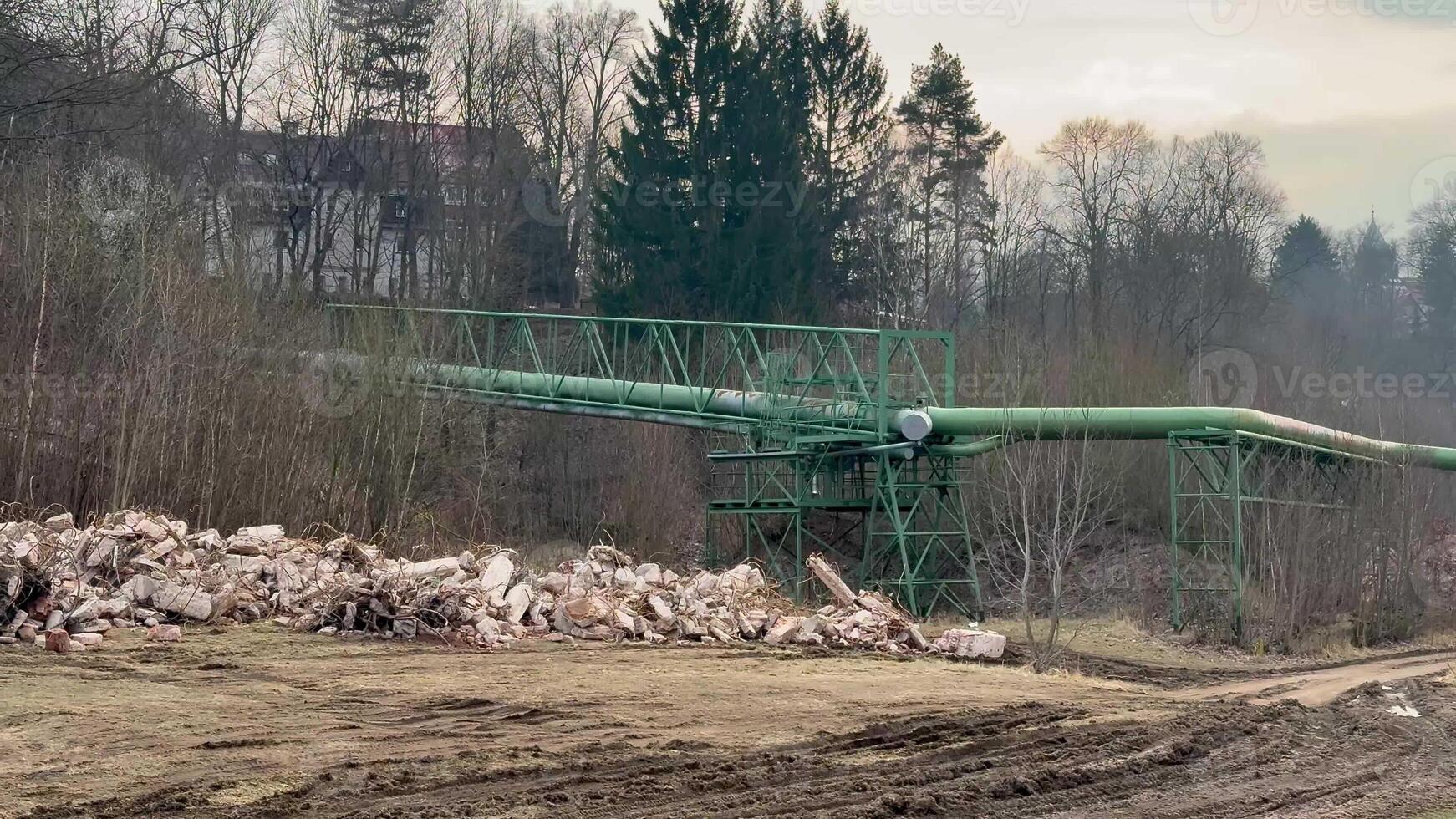 A long green conveyor bridge stretches across an industrial site, with assorted debris scattered in the foreground photo