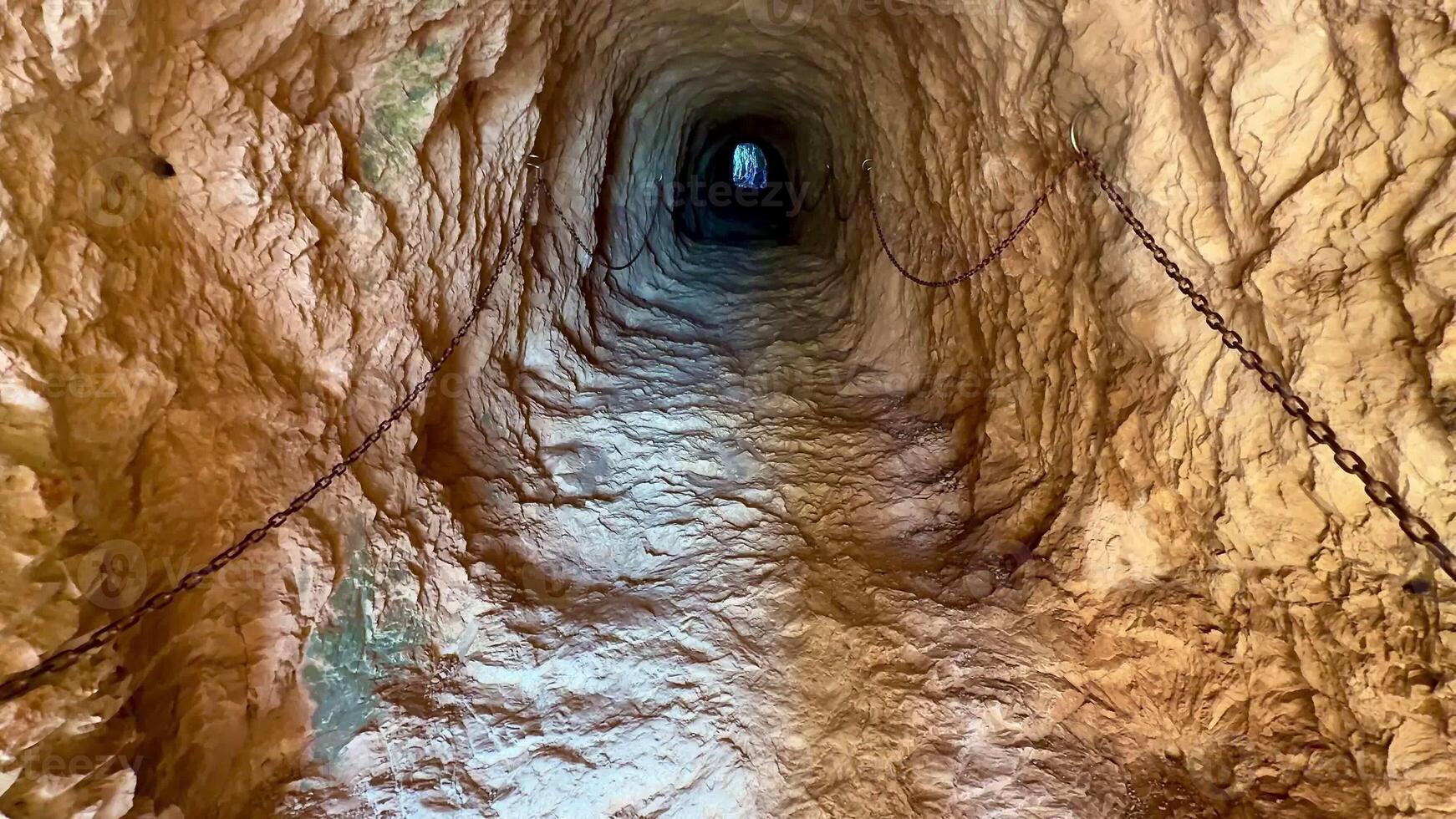 A captivating view of an ancient, mysterious tunnel featuring beautifully textured walls and a bright light at the end photo