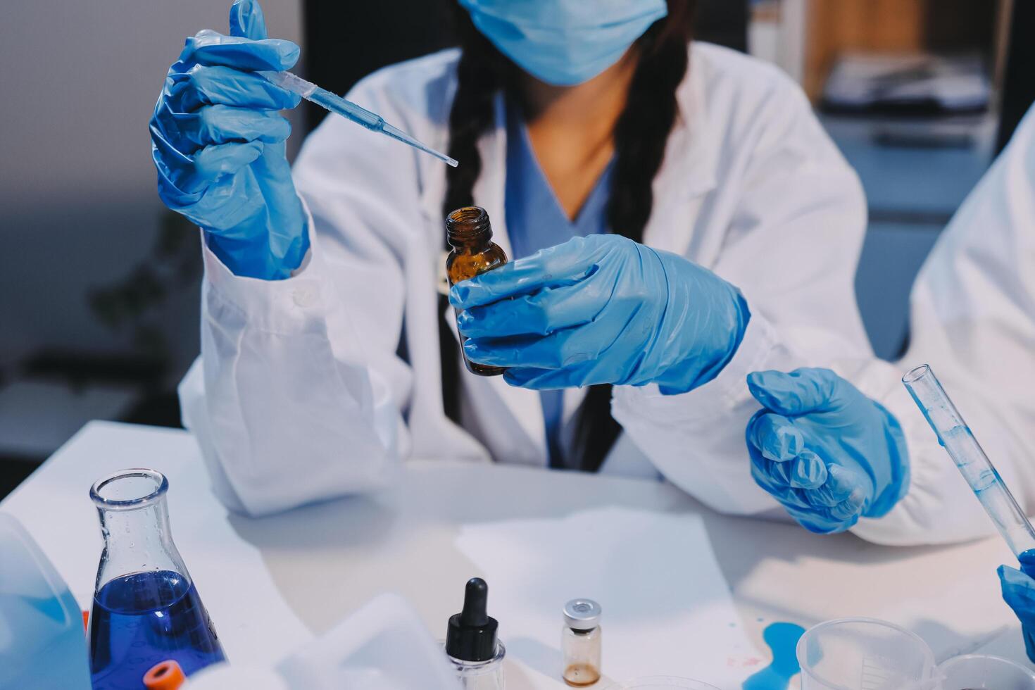 Two people in lab coats and gloves holding a vial photo