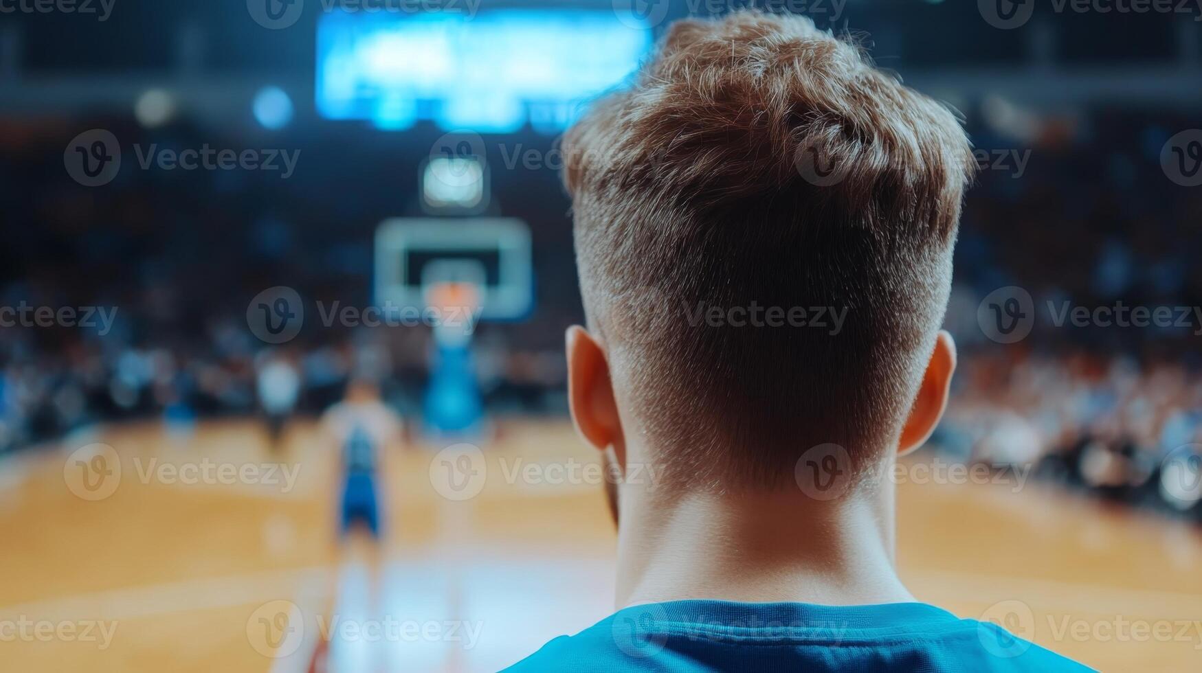 Young athlete watching basketball game from sidelines in a vibrant arena at night during a competitive match photo