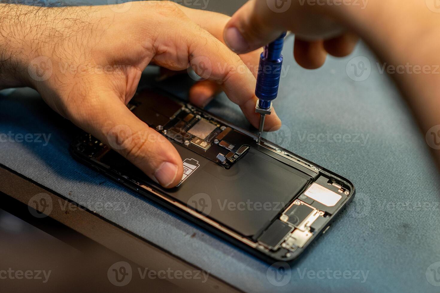 Smartphone Repair in Progress With Technician Using Screwdriver on Device at Busy Workshop photo