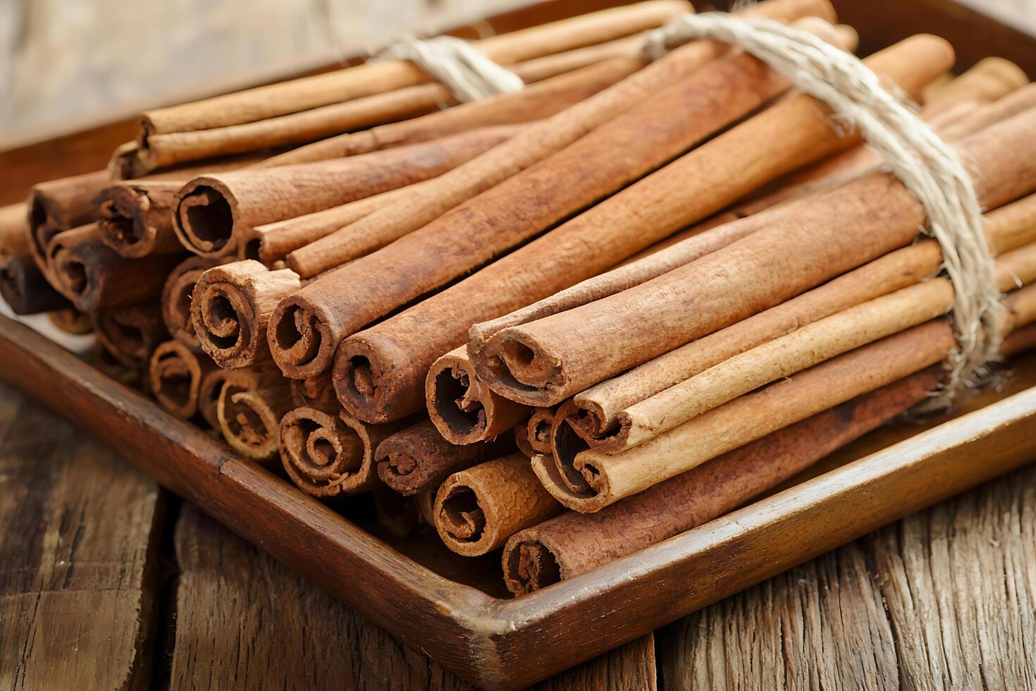 Aromatic Cinnamon Sticks Bundled in Rustic Wooden Tray. A close-up image of fragrant cinnamon sticks tied together with twine, resting on a weathered wooden surface. photo