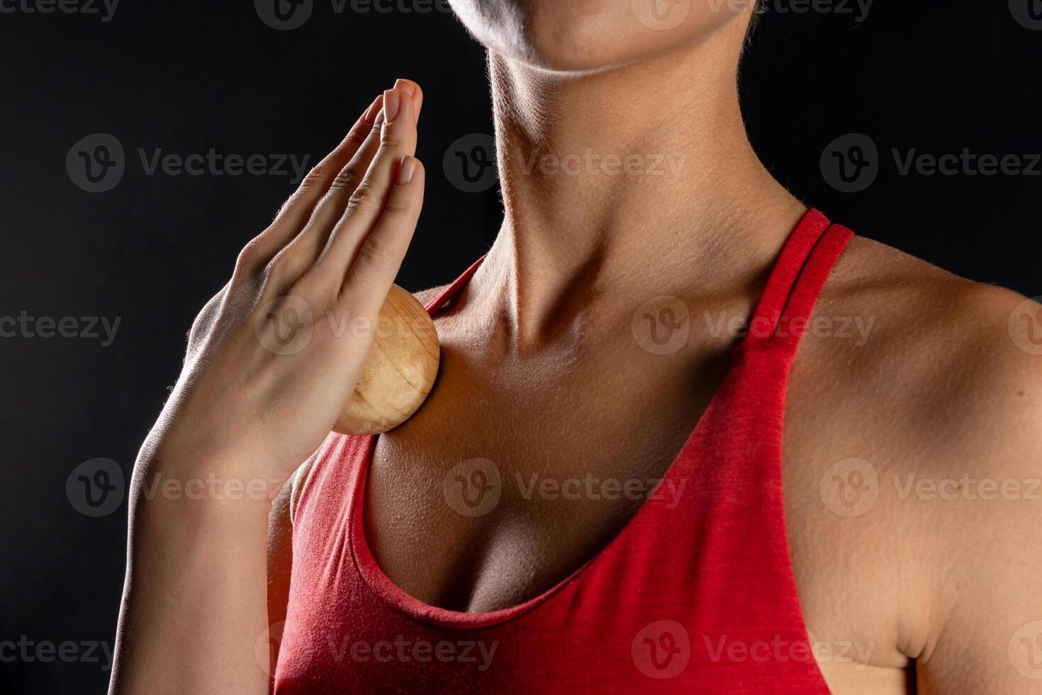 Close up of woman using wooden massage ball on chest wearing red tank top on dark background, self care and relaxation techniques. self massage tool photo