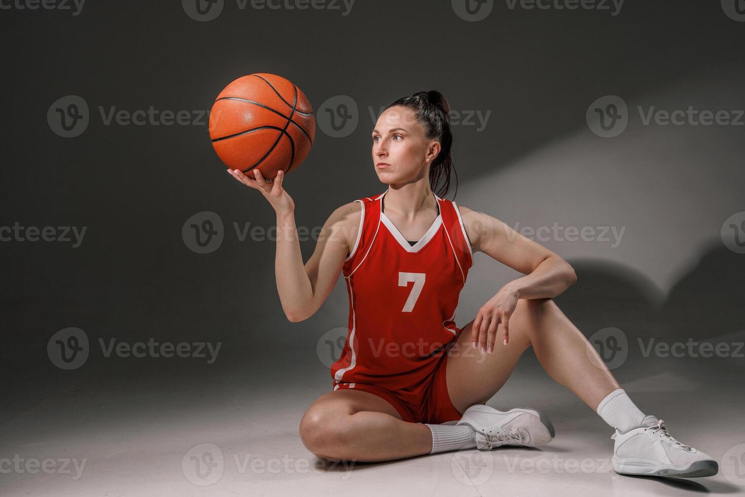Confident Female Basketball Player Sitting with Ball in Red Uniform after Training on Court photo