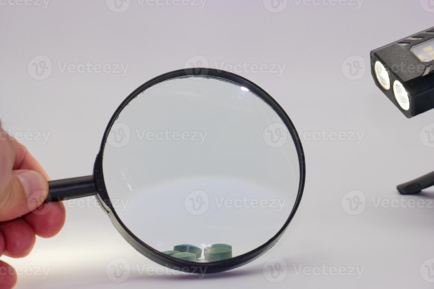 Magnifying glass held by a person near a light source and small objects on a surface in a well lit environment photo