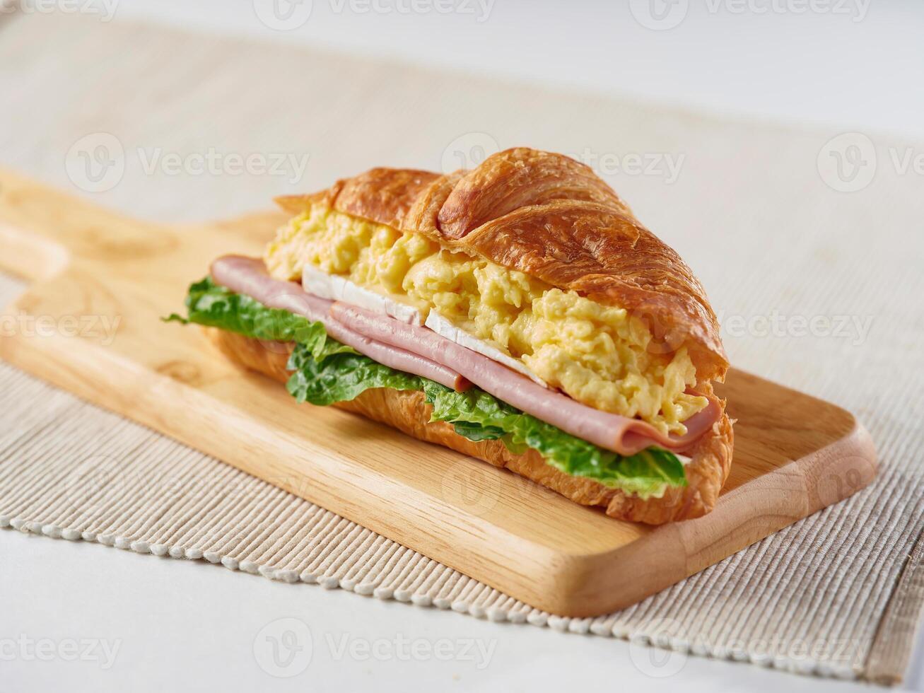 Scrambled Egg, Brie Cheese and Ham Croissant with lettuce on wooden board side view of breakfast menus photo