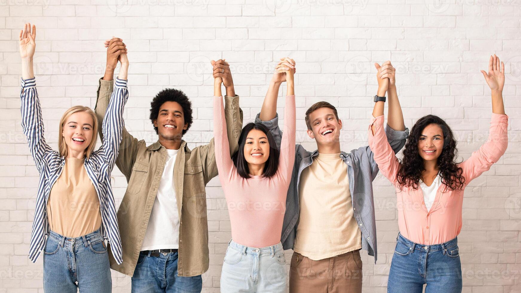 Teamwork, support from friend in studies and emotions of success. Cheerful digital young international people hold hands and lift up and have fun, on white wall background, studio shot, empty space photo