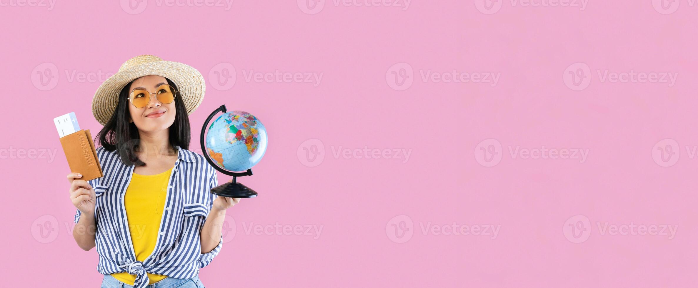 Dream Vacation. Portrait of excited happy asian woman traveller holding passport with plane boarding pass tickets and globe, wearing sunglasses, looking up and dreaming about trip, pink studio wall photo