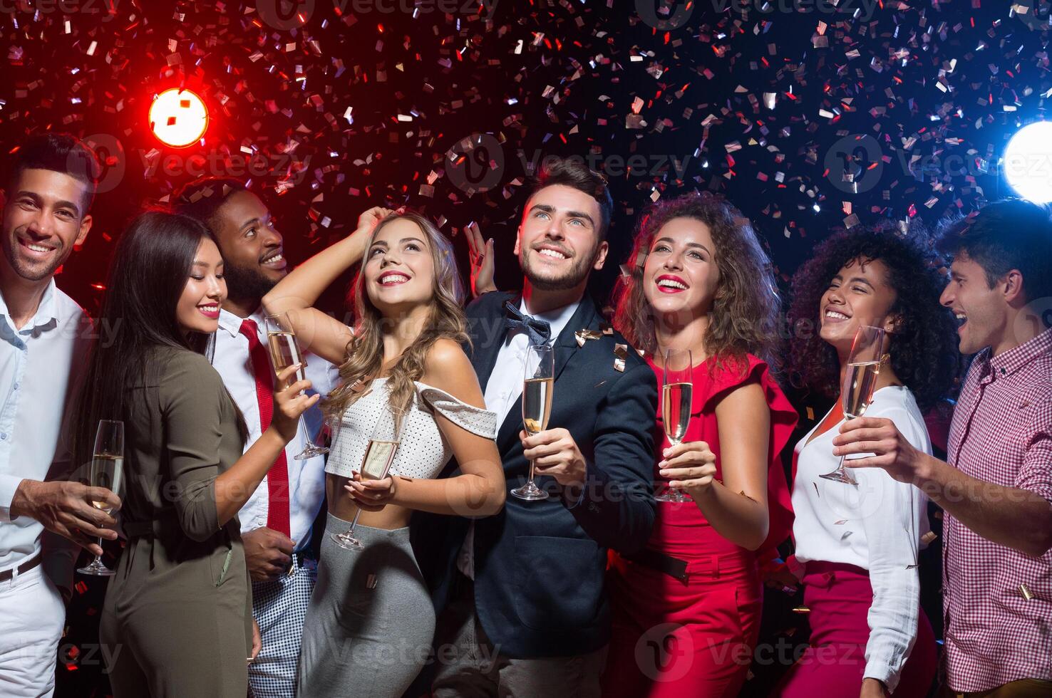 Cheerful friends with champagne flutes dancing at New Year party, smiling upwards at camera photo