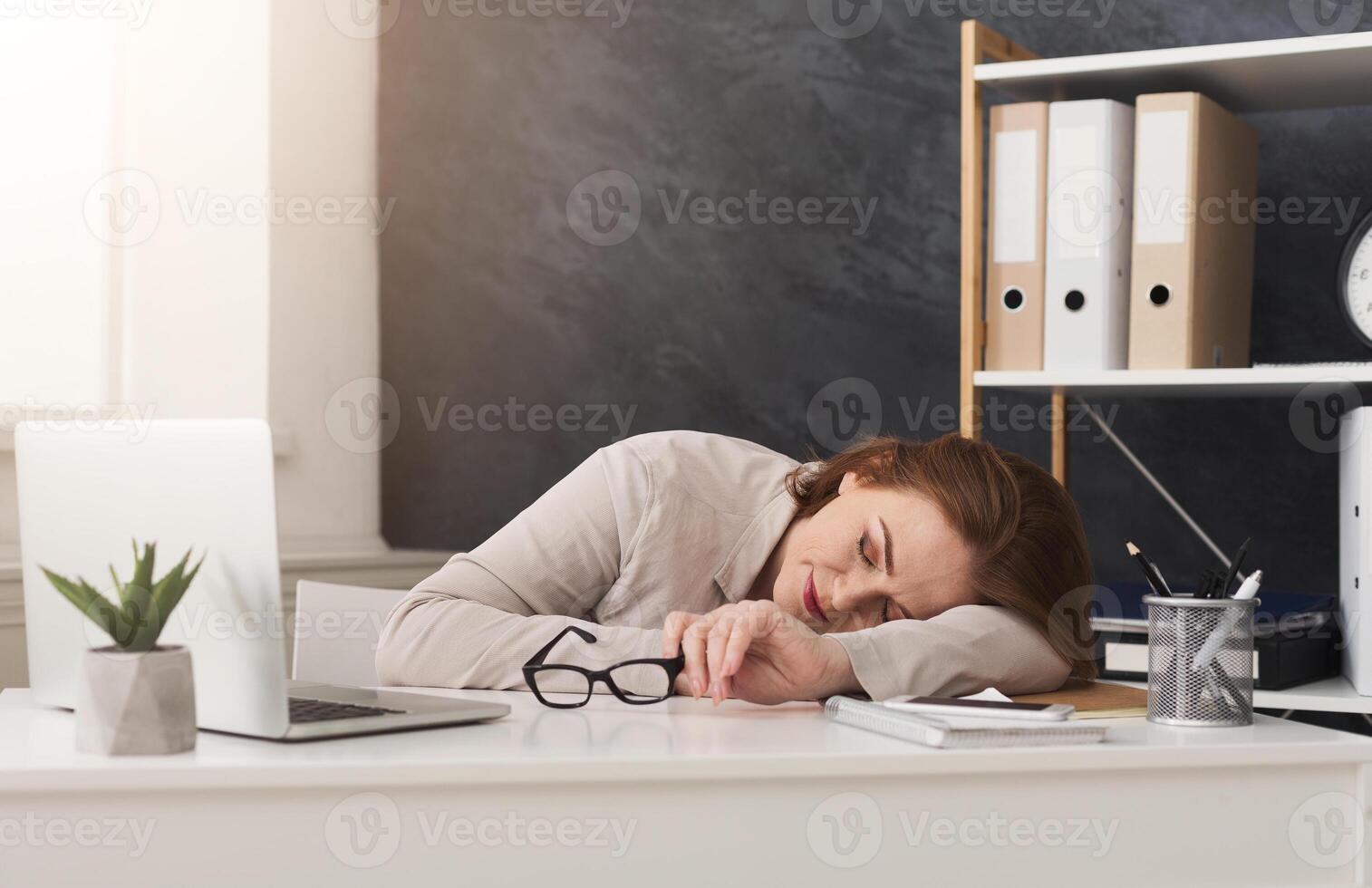 Tired middle aged businesswoman sleeping on her workplace while working on laptop in office photo