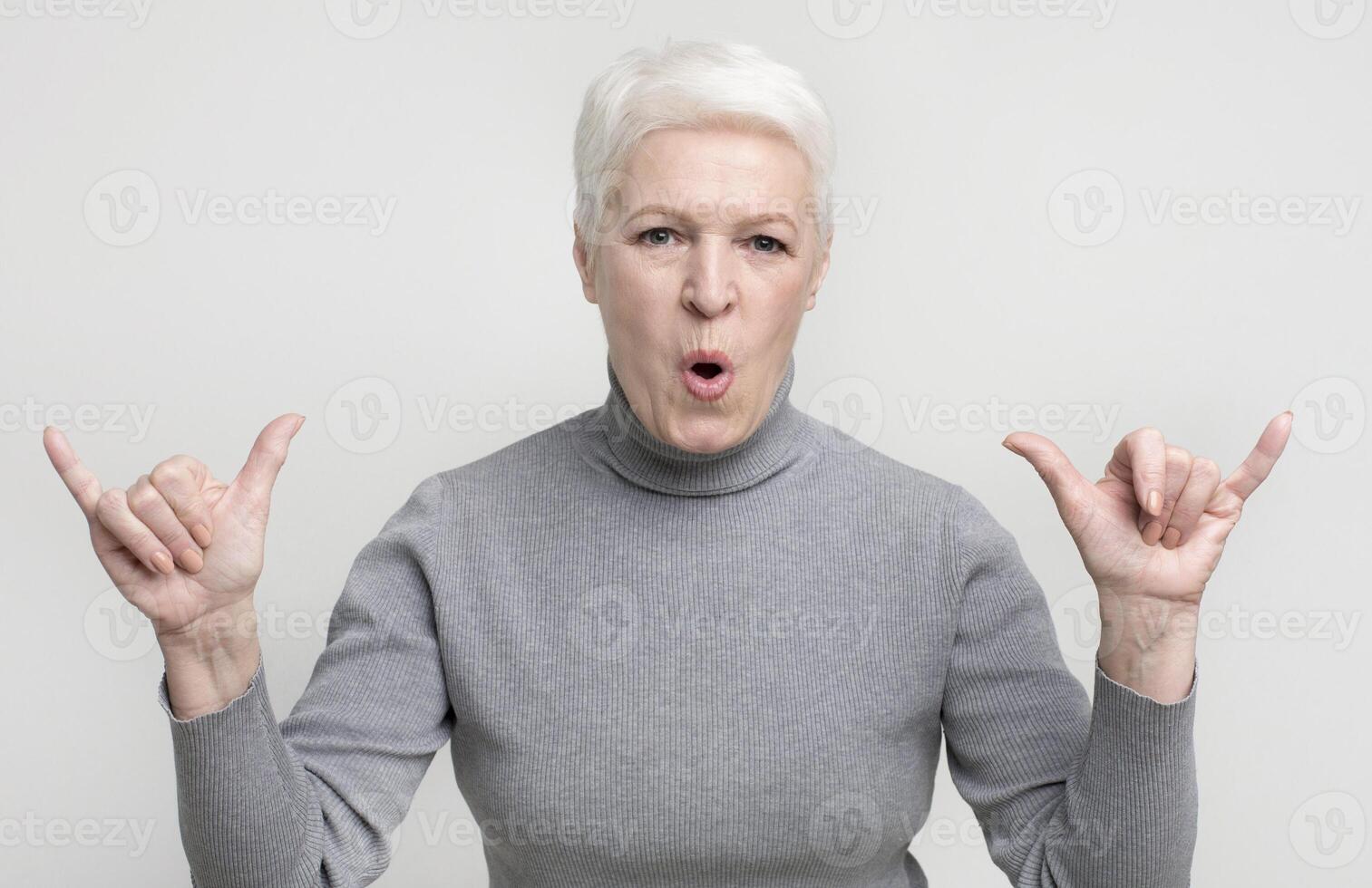 Cool grandmother showing modern trendy rock gesture on light studio background, copy space photo