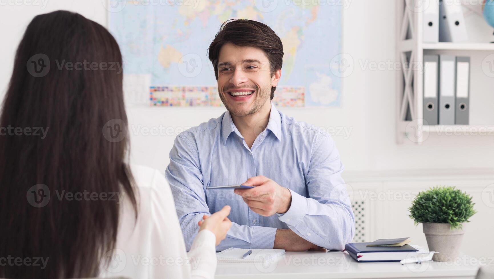 Getting visa. Male travel agent giving passport to tourist in office photo