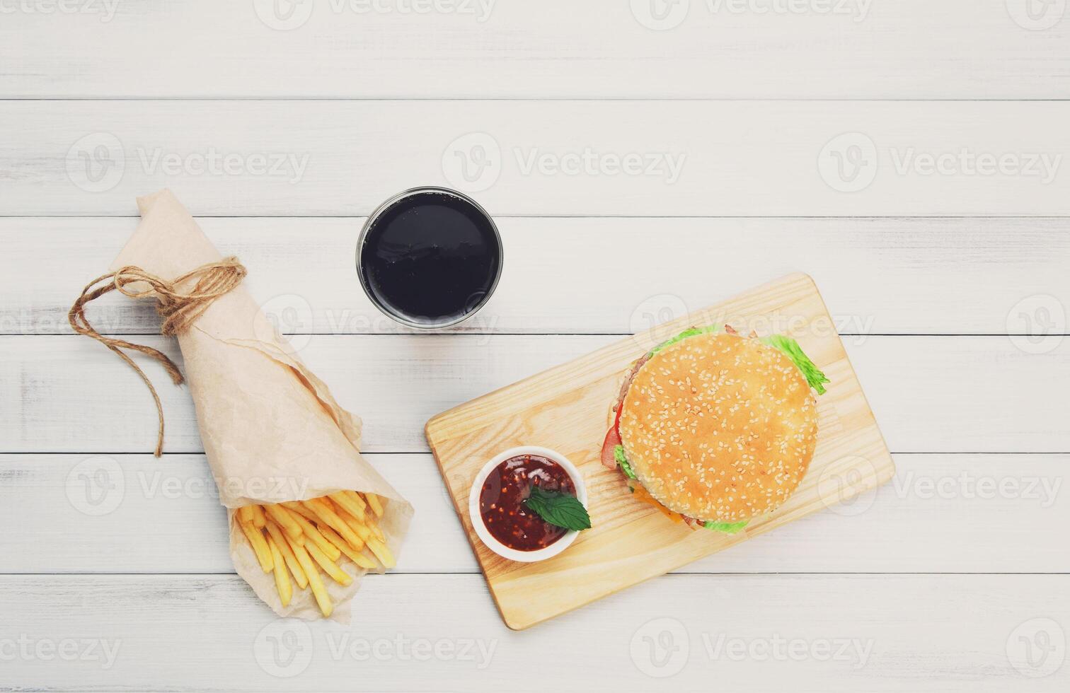Burger, Chips and cola. Hamburger and french fries wrapped in brown wrapping paper. Fast food take away at white shabby chic wood. Hamburger with tomato sauce. Top view, flat lay with copyspace photo