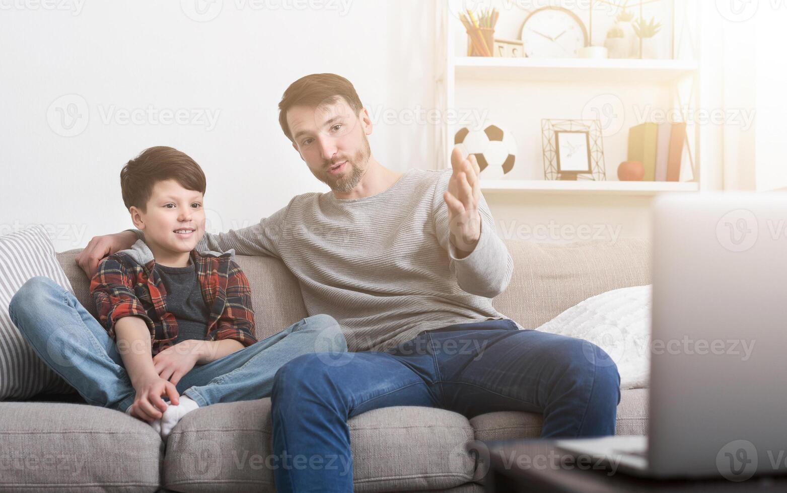 Happy father and son watching a movie on a laptop, sitting on a sofa at home photo