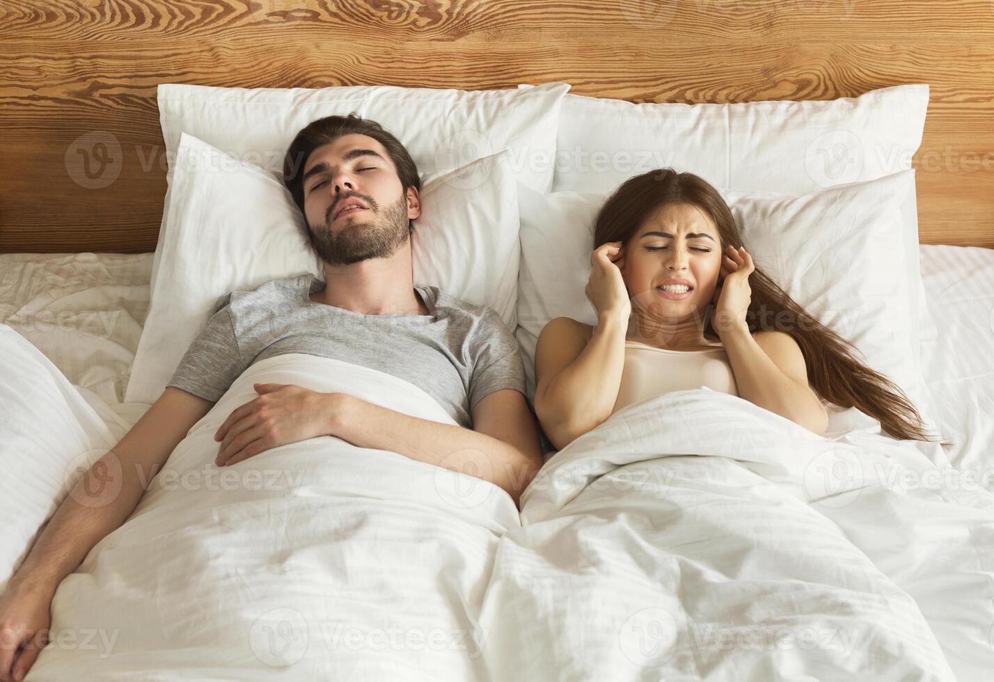 Snoring husband. Angry woman covering ears in bed. photo
