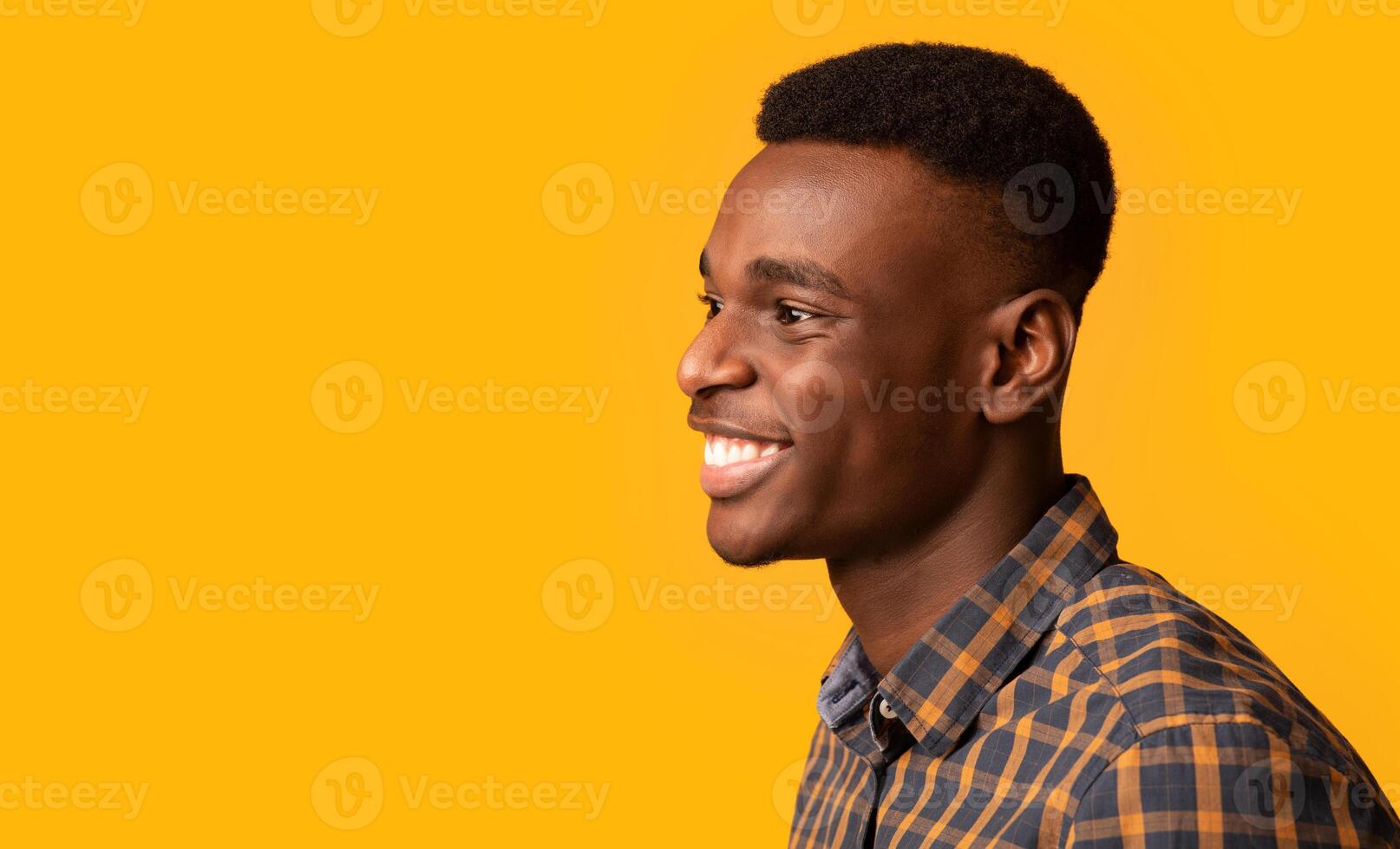Side view shot of joyful millennial African American guy isolated over yellow background, profile view of handsome black young man sincerely smiling and looking away, panorama with copy space photo