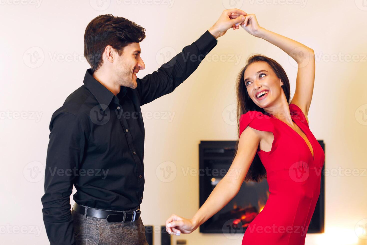Love And Affection. Portrait of smiling millennial man in black shirt and woman in red dress dancing. Happy young couple enjoying spending time together at a party at home, celebrating event photo