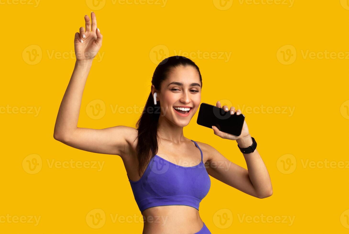 Music Lover. Portrait Of Cheerful Happy Sporty Woman Wearing Wireless Earbuds, Holding Smartphone As Mic And Singing, Listening To Favourite Playlist Isolated On Orange Studio Background photo