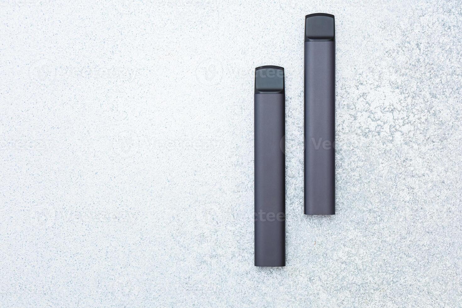 Two sleek vape devices on a textured gray surface captured in a minimalist style photo