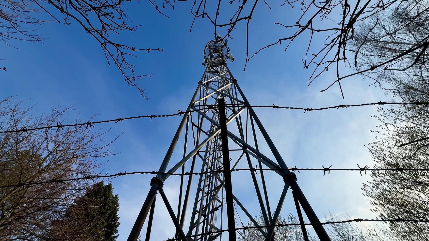 A striking and captivating view of a large communication tower secured tightly by barbed wire against a clear blue sky photo