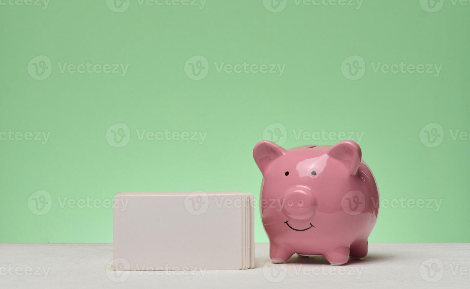 Pink ceramic piggy bank and stack of white business cards on green background photo