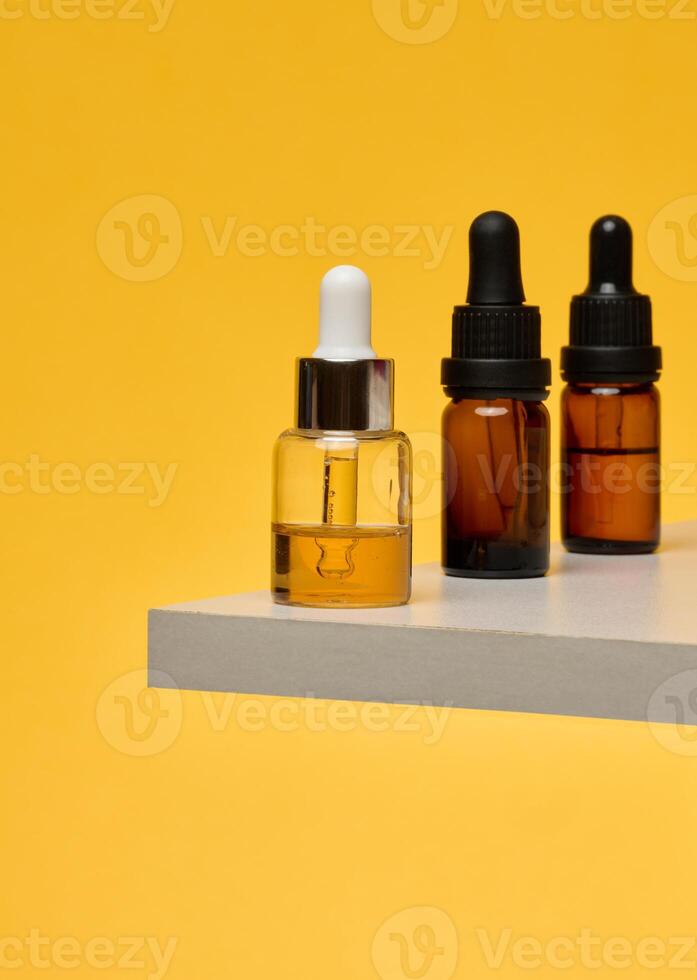 Cosmetic bottles with pipettes on a stone stand. Stylish composition for skin care, oils and serums on a bright yellow background. photo