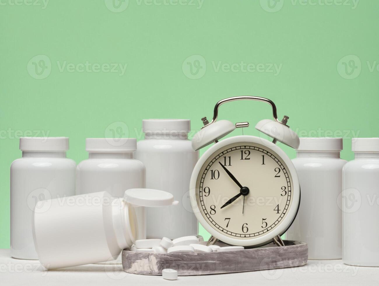A set of white plastic pill bottles and an alarm clock are placed on a green background. photo