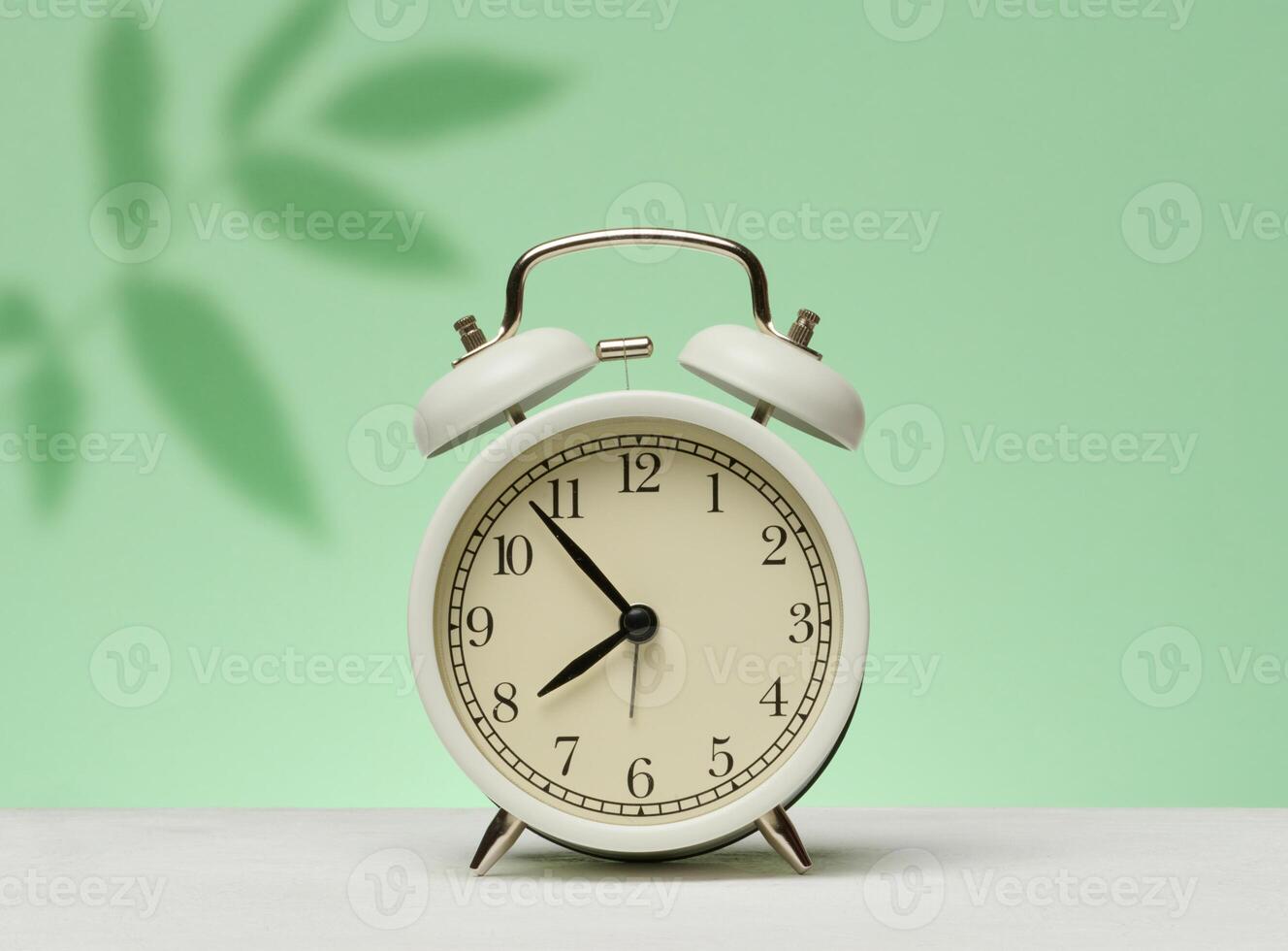 White vintage alarm clock stands on a green surface against a background with shadows from leaves. Waking up and starting the day. photo