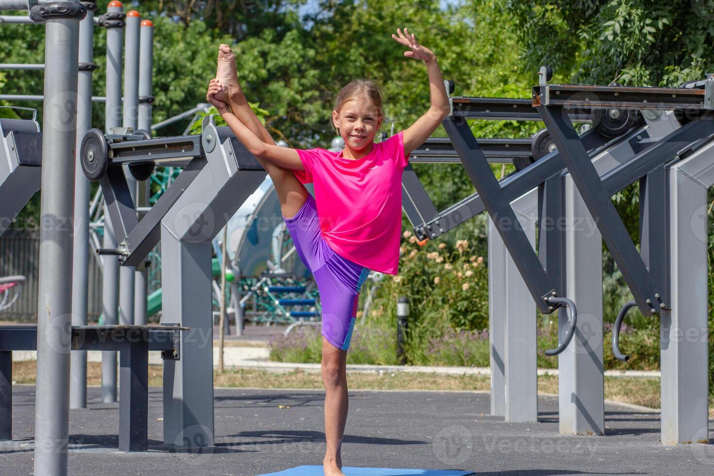 A child balancing on one leg while holding the other leg raised high, demonstrating flexibility and balance through a stretching pose photo