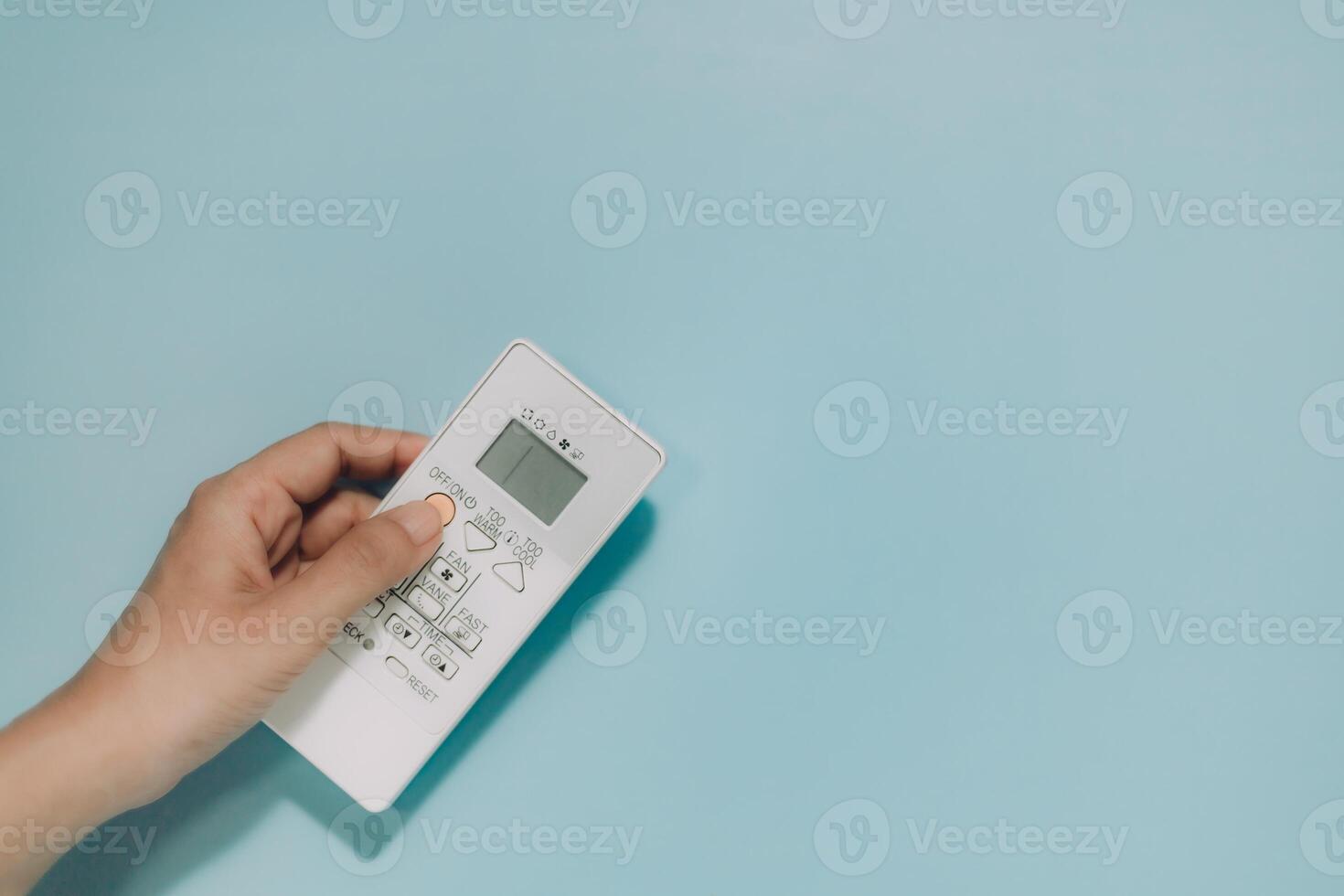 Hand holding a white AC remote, fingers on buttons, against light blue. Ideal for climate control, comfort, technology, and home appliances. photo