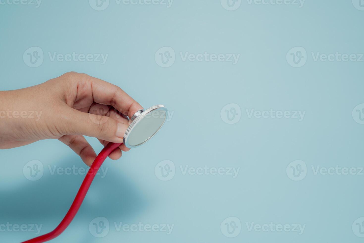 Hand holding a red stethoscope diaphragm on light blue. Symbolizes health check-ups, medical consultations, and general healthcare. photo