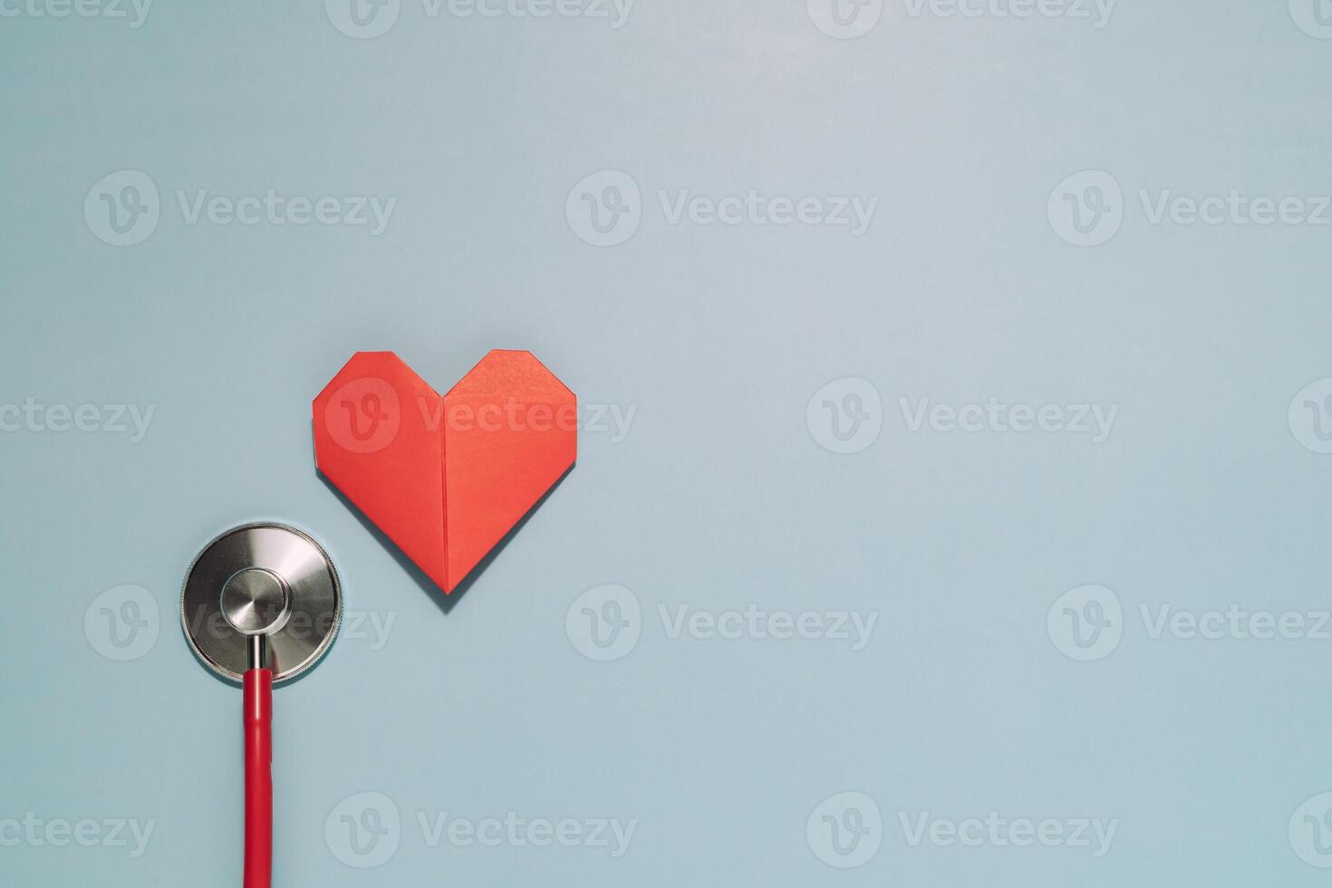Vibrant red origami heart next to a red stethoscope diaphragm on light blue. Powerfully symbolizes heart health, cardiology, medical care, and love for life. photo
