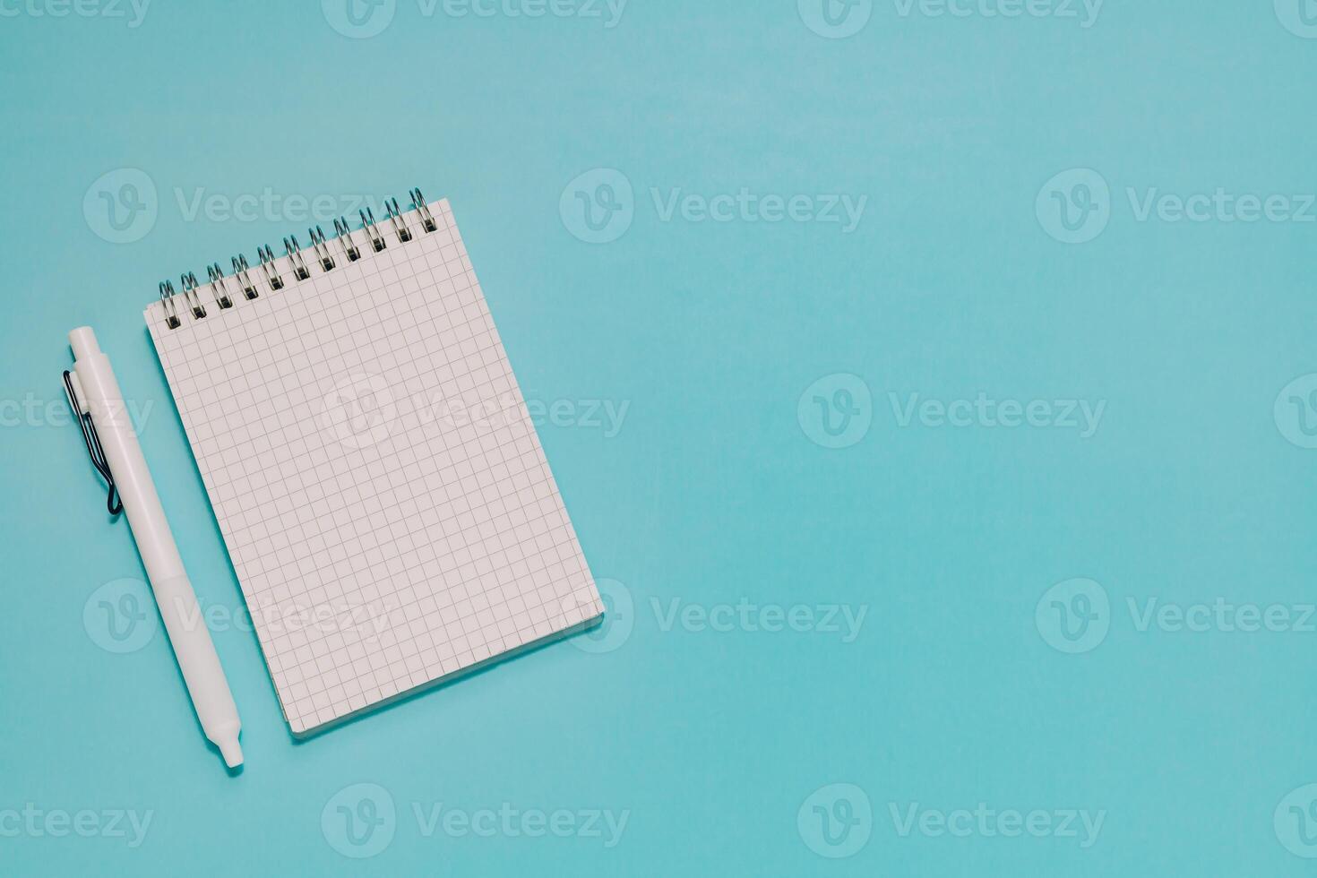 Blank grid notepad and white pen neatly arranged on vibrant blue. Ideal for planning, writing, study, note-taking, and professional workspace. photo