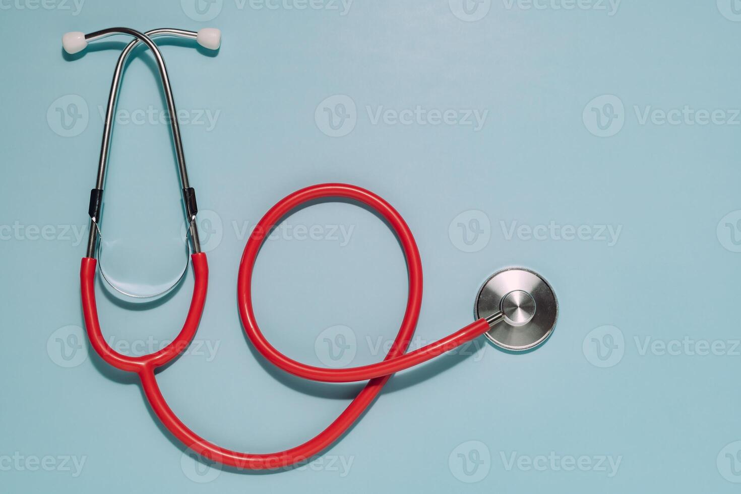 Vibrant red stethoscope, earpieces top, diaphragm right, on light blue. Ideal for healthcare, medical care, diagnosis, and general health awareness. photo