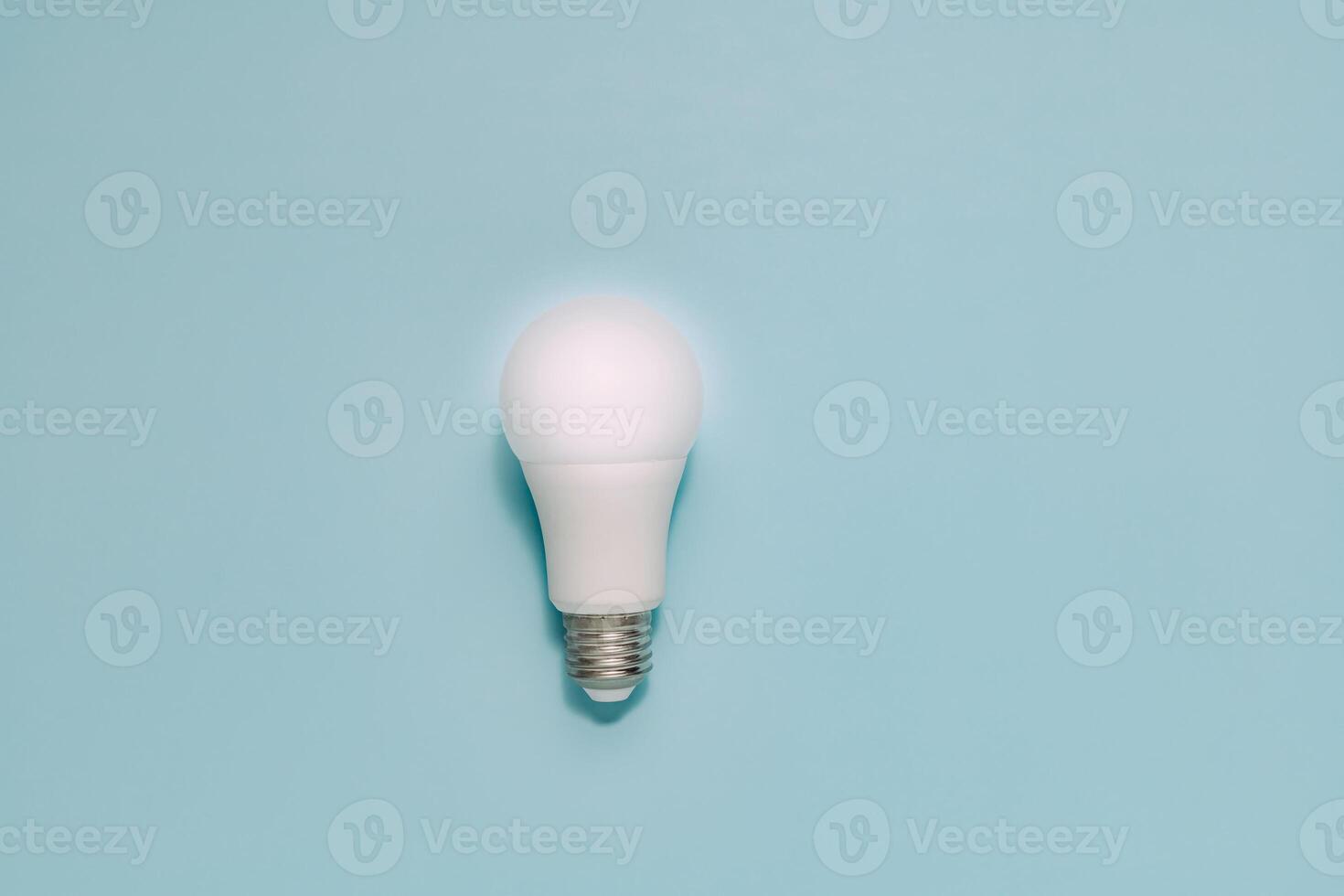 Single white LED light bulb stands upright on smooth, muted blue. Symbolizes ideas, innovation, energy efficiency, and sustainable technology. photo