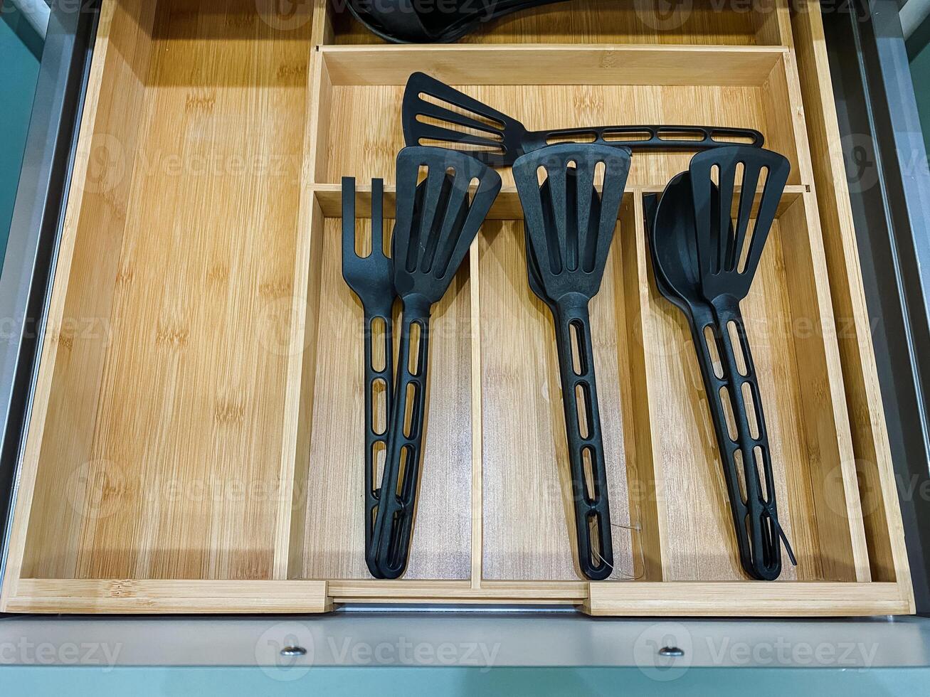 In a wellorganized wooden drawer, there are various black spatulas and spoons, all ready for use, highlighting the blend of functionality and aesthetics in this household space photo