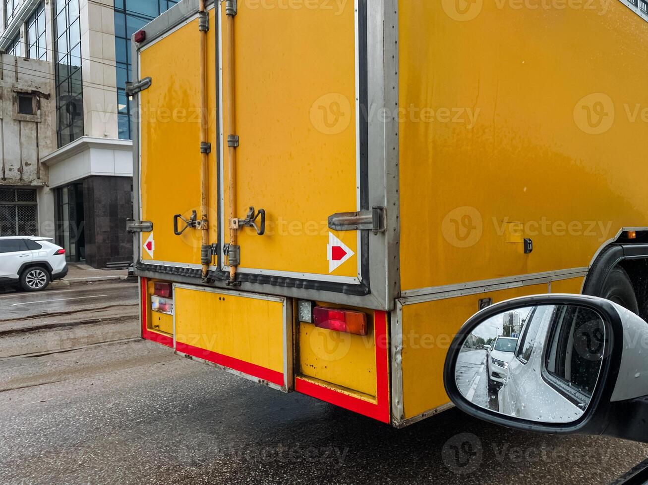 This closeup shows a vibrant yellow delivery truck with bright reflective markings in a bustling urban setting, highlighting its essential role in the citys logistics and transportation photo