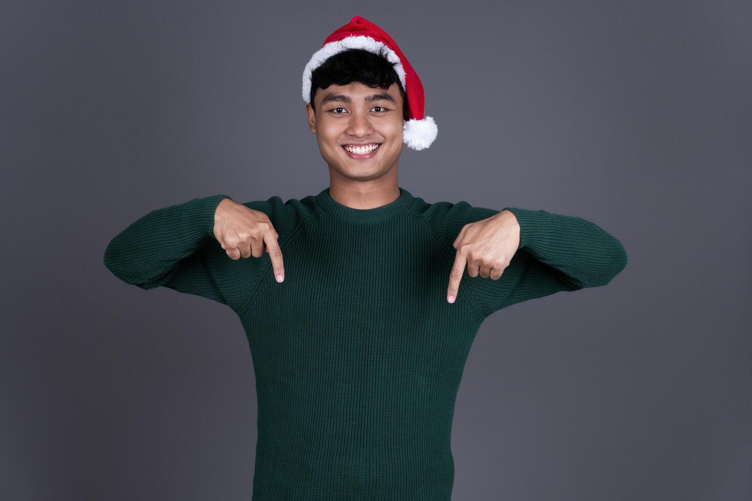 Portrait of Happy Young Asian Man Pointing Down Wearing Santa Hat, Christmas Holiday Concept photo