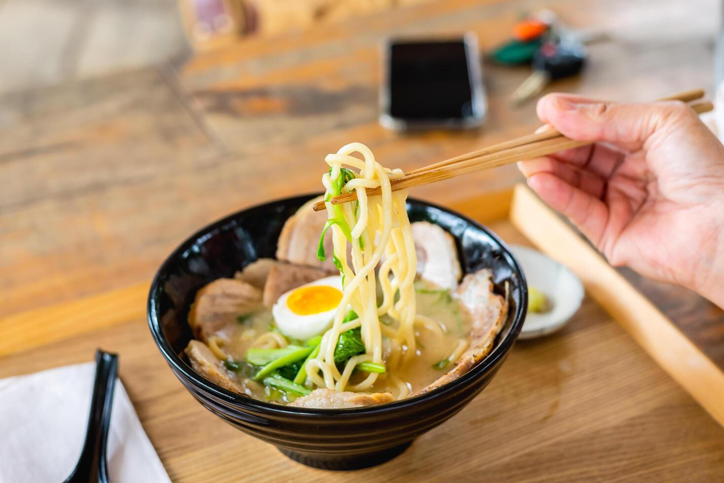 Hand of woman eating a ramen Japanese noodle soup in a black color ramen bowl. photo
