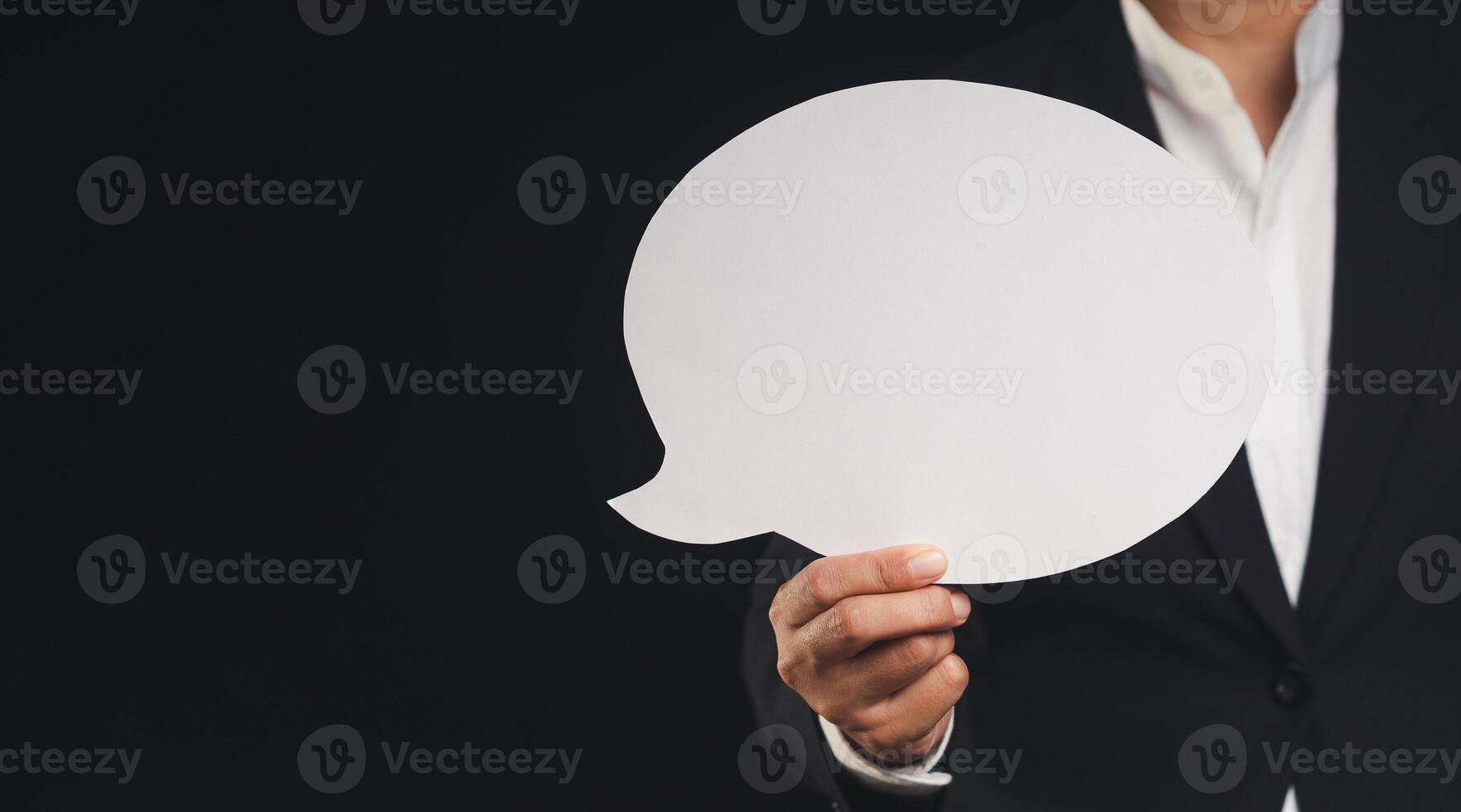 Close-up of a businessman holding a blank white speech bubble while standing on a black background. photo